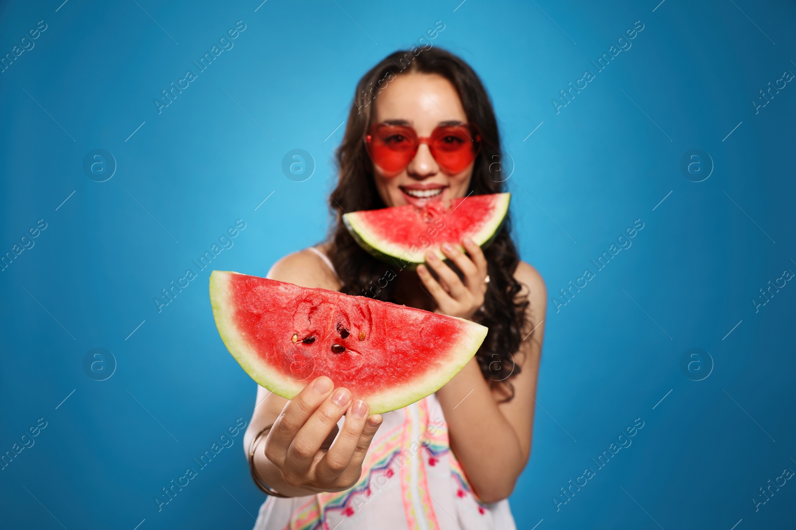 Photo of Beautiful young woman against blue background, focus on hand with watermelon