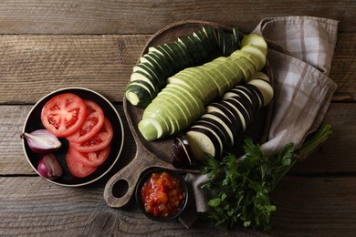 Photo of Cooking delicious ratatouille. Different cut vegetables, parsley and plate on wooden table, flat lay