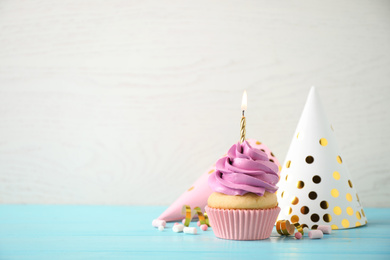 Delicious birthday cupcake with burning candle on light blue wooden table. Space for text