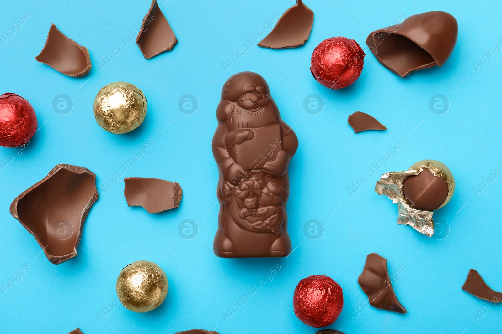 Photo of Flat lay composition with whole and broken chocolate Santa Claus candies on light blue background