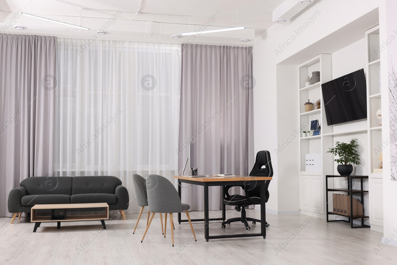 Photo of Stylish director's workplace with wooden table, tv zone, shelves and comfortable armchairs in room. Interior design