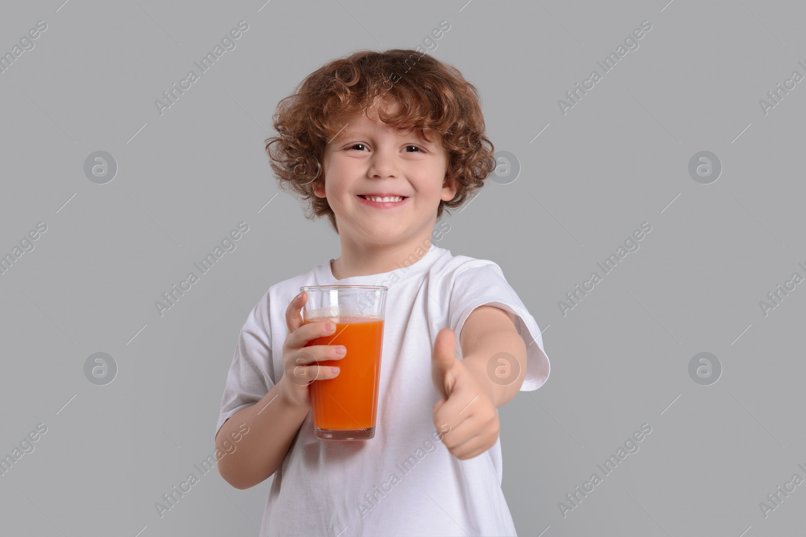 Photo of Cute little boy with glass of fresh juice showing thumb up on light gray background