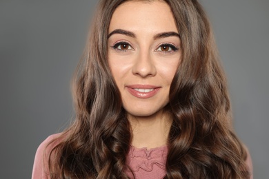 Beautiful woman with shiny wavy hair on grey background