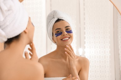 Beautiful young woman with under eye patches near mirror at home