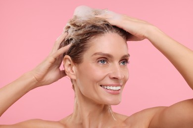 Beautiful happy woman washing hair on pink background