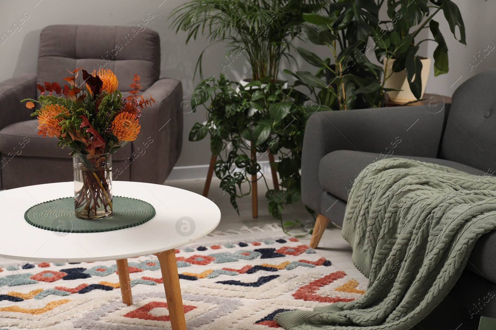 Photo of Vase with bouquet of beautiful leucospermum flowers on coffee table, sofa, armchair and houseplants in room