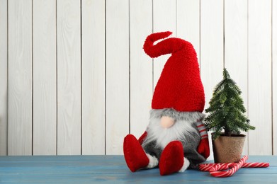 Photo of Cute Christmas gnome, small decorative fir tree and candy canes on turquoise table against white wooden background. Space for text