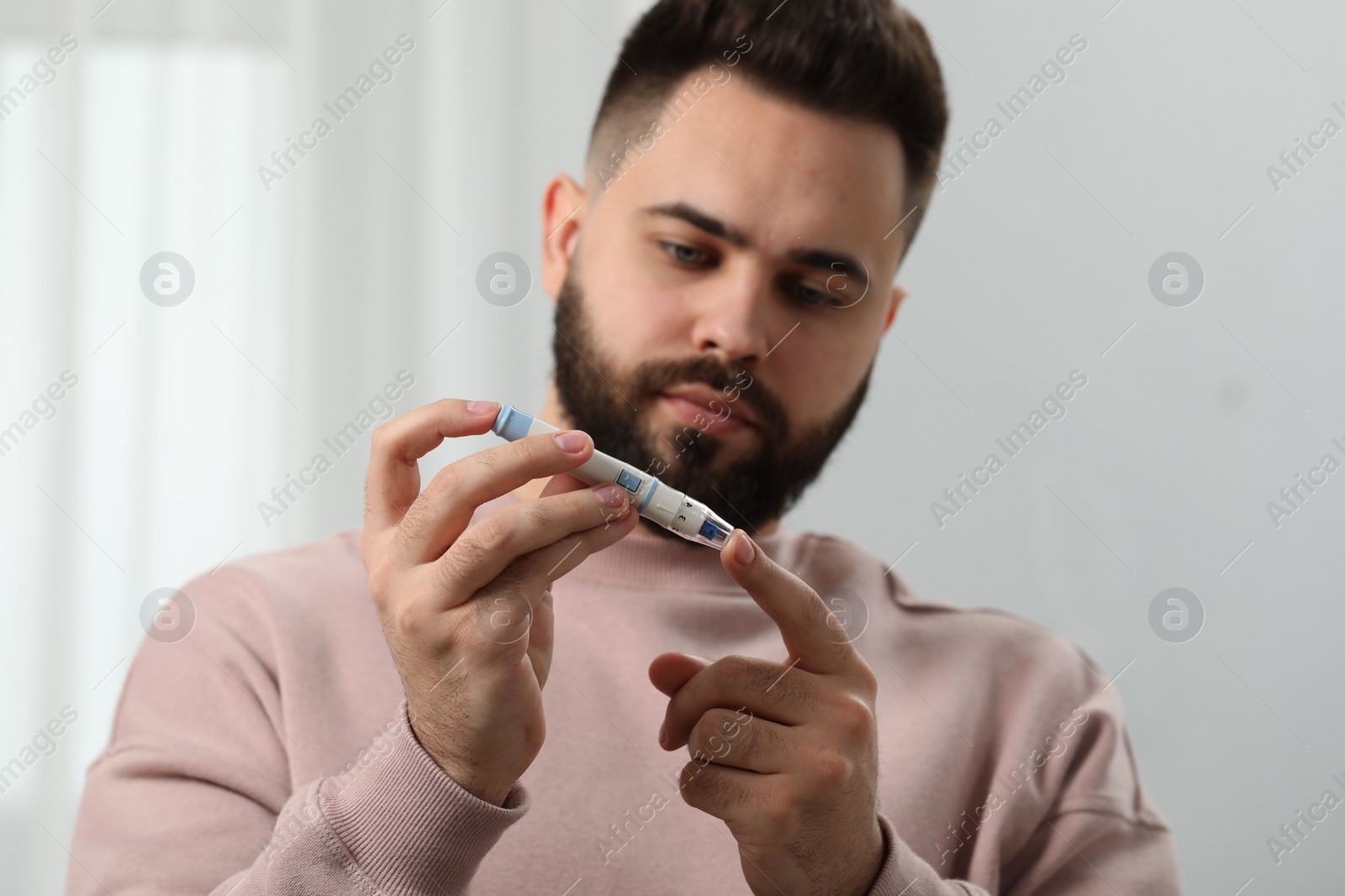 Photo of Diabetes test. Man checking blood sugar level with lancet pen at home, selective focus