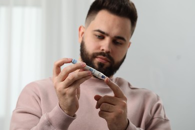 Photo of Diabetes test. Man checking blood sugar level with lancet pen at home, selective focus