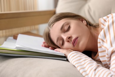 Photo of Young tired woman sleeping near books on couch indoors, closeup