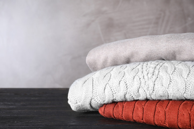 Image of Stack of folded warm sweaters on black wooden table. Space for text