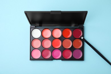 Photo of Cream lipstick palette and brush on light turquoise background, flat lay. Professional cosmetic product