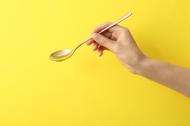 Photo of Woman holding empty table spoon on color background, closeup