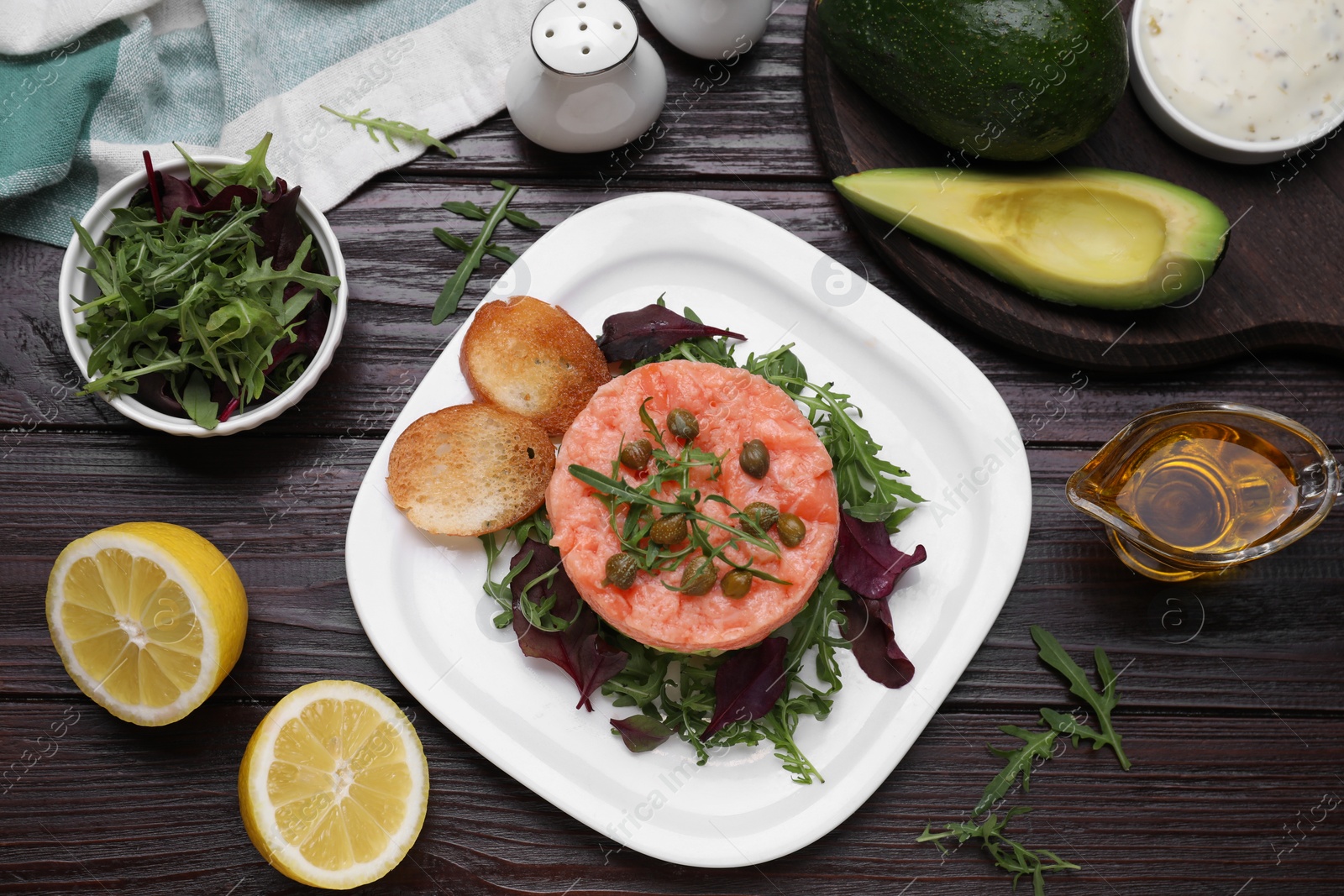 Photo of Tasty salmon tartare with greens and croutons on wooden table, flat lay