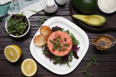 Tasty salmon tartare with greens and croutons on wooden table, flat lay