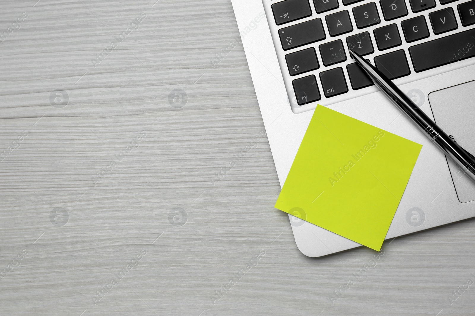 Photo of Laptop with blank sticky note and pen on white wooden table, top view. Space for text