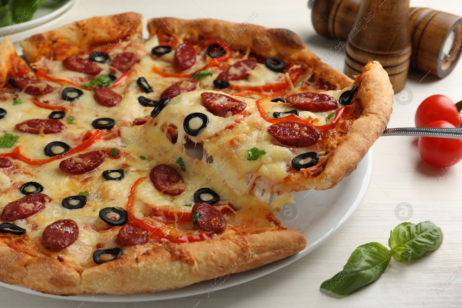 Photo of Taking piece of tasty pizza with smoked sausages, olives, pepper and parsley at light wooden table, closeup