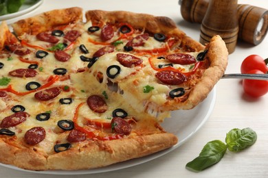 Photo of Taking piece of tasty pizza with smoked sausages, olives, pepper and parsley at light wooden table, closeup