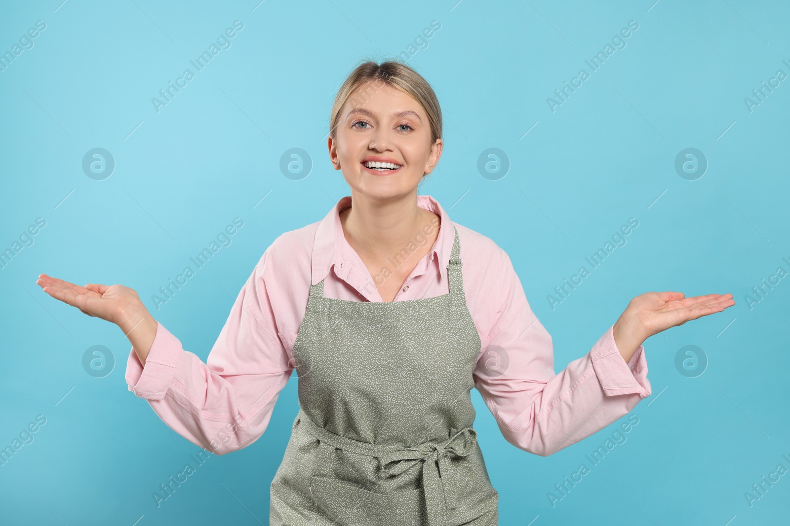 Photo of Beautiful young woman in clean apron with pattern on light blue background