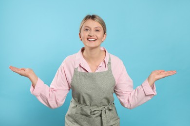 Beautiful young woman in clean apron with pattern on light blue background