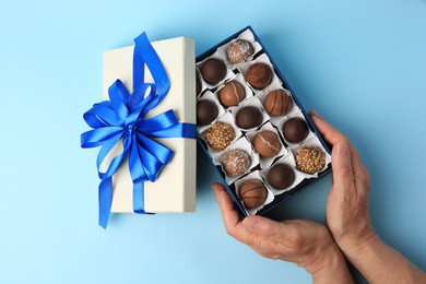 Photo of Woman with box of delicious chocolate candies on light blue background, top view