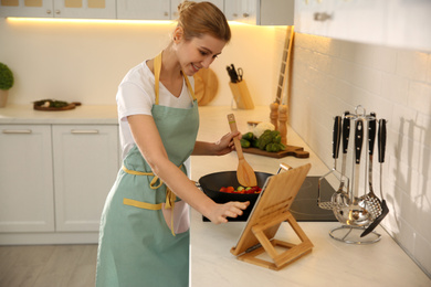 Photo of Young woman with tablet cooking on stove in kitchen
