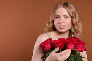 Photo of Beautiful woman with blonde hair holding bouquet of red roses on brown background. Space for text
