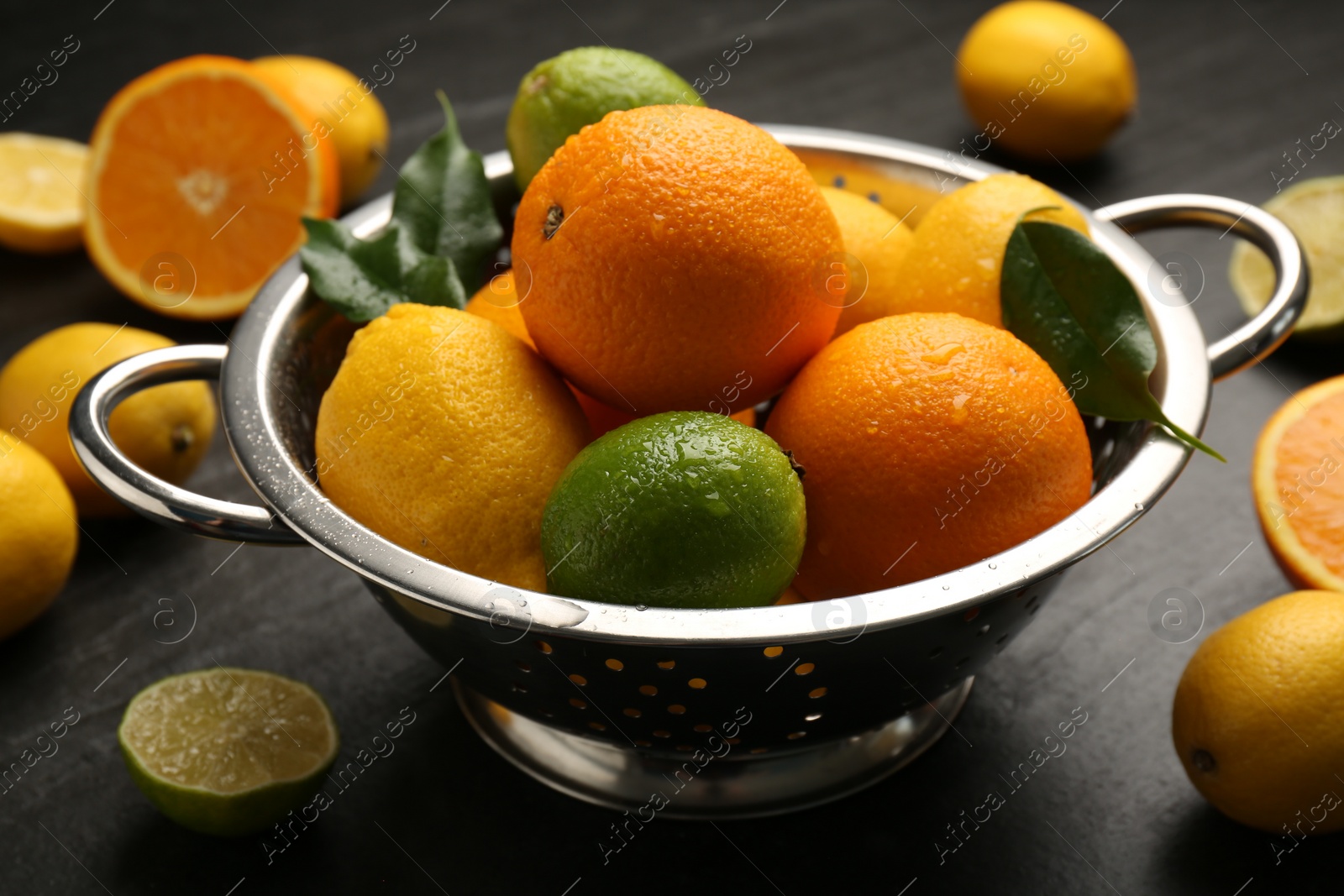 Photo of Fresh citrus fruits in colander on dark table, closeup