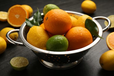 Photo of Fresh citrus fruits in colander on dark table, closeup