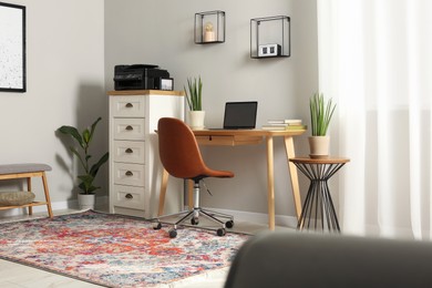Photo of Stylish room interior with chest of drawers, modern printer and laptop