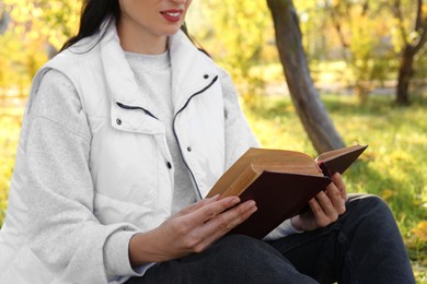 Photo of Woman reading book in park on autumn day, closeup
