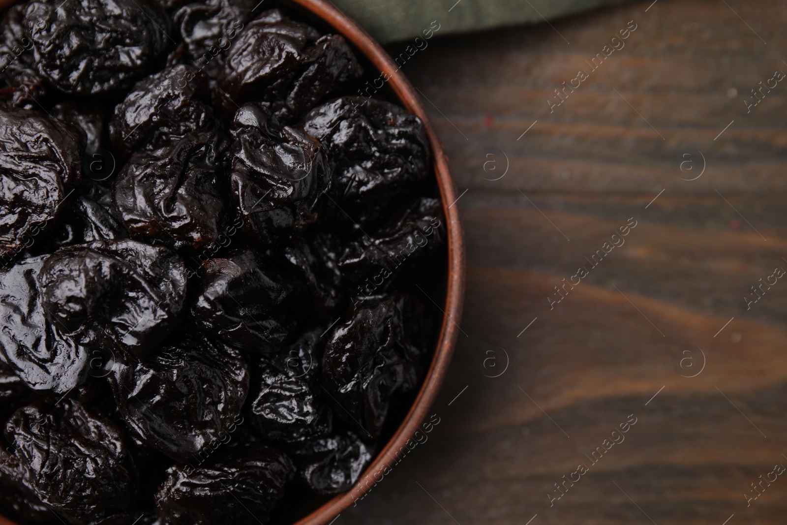 Photo of Sweet dried prunes in bowl on wooden table, top view. Space for text