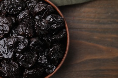 Sweet dried prunes in bowl on wooden table, top view. Space for text