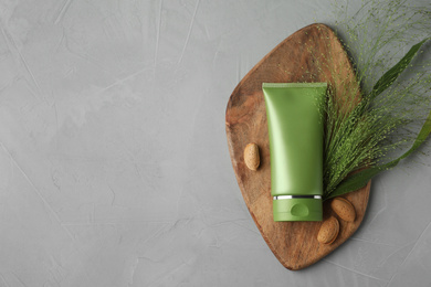 Photo of Tube of cosmetic product, plant and almond nuts on grey table, flat lay. Space for text