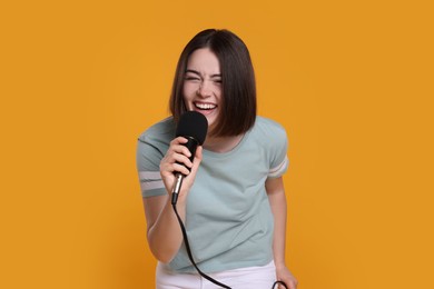 Photo of Beautiful young woman with microphone singing on yellow background