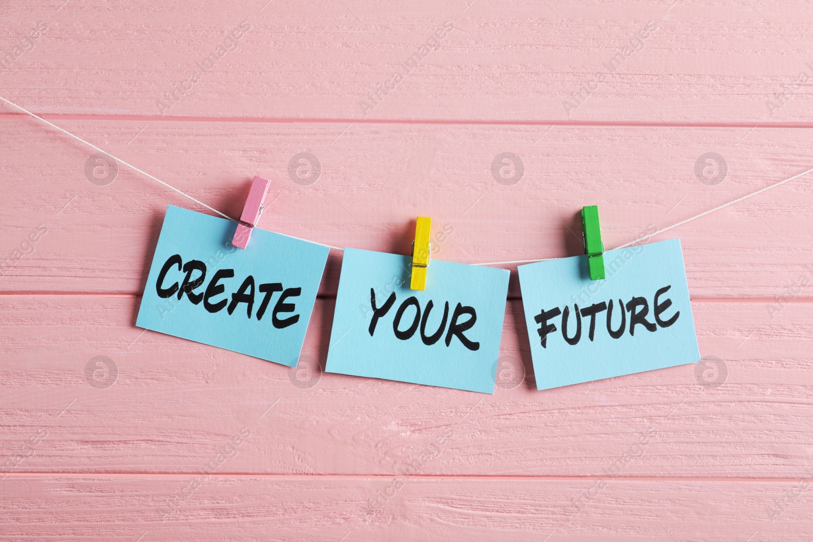 Photo of Paper notes with motivational phrase Create Your Future hanging on pink wooden wall
