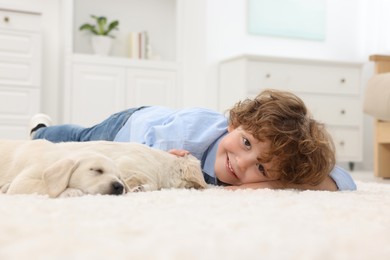 Photo of Little boy lying with cute puppies on white carpet at home