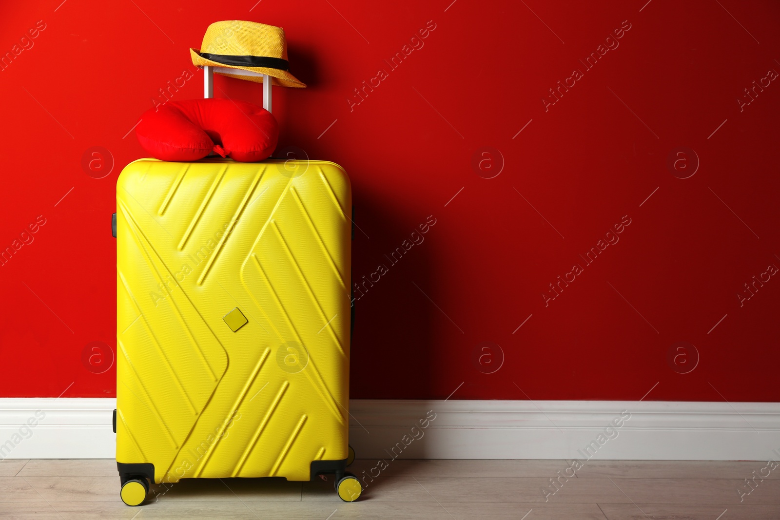 Photo of Yellow suitcase, hat and travel pillow near red wall, space for text