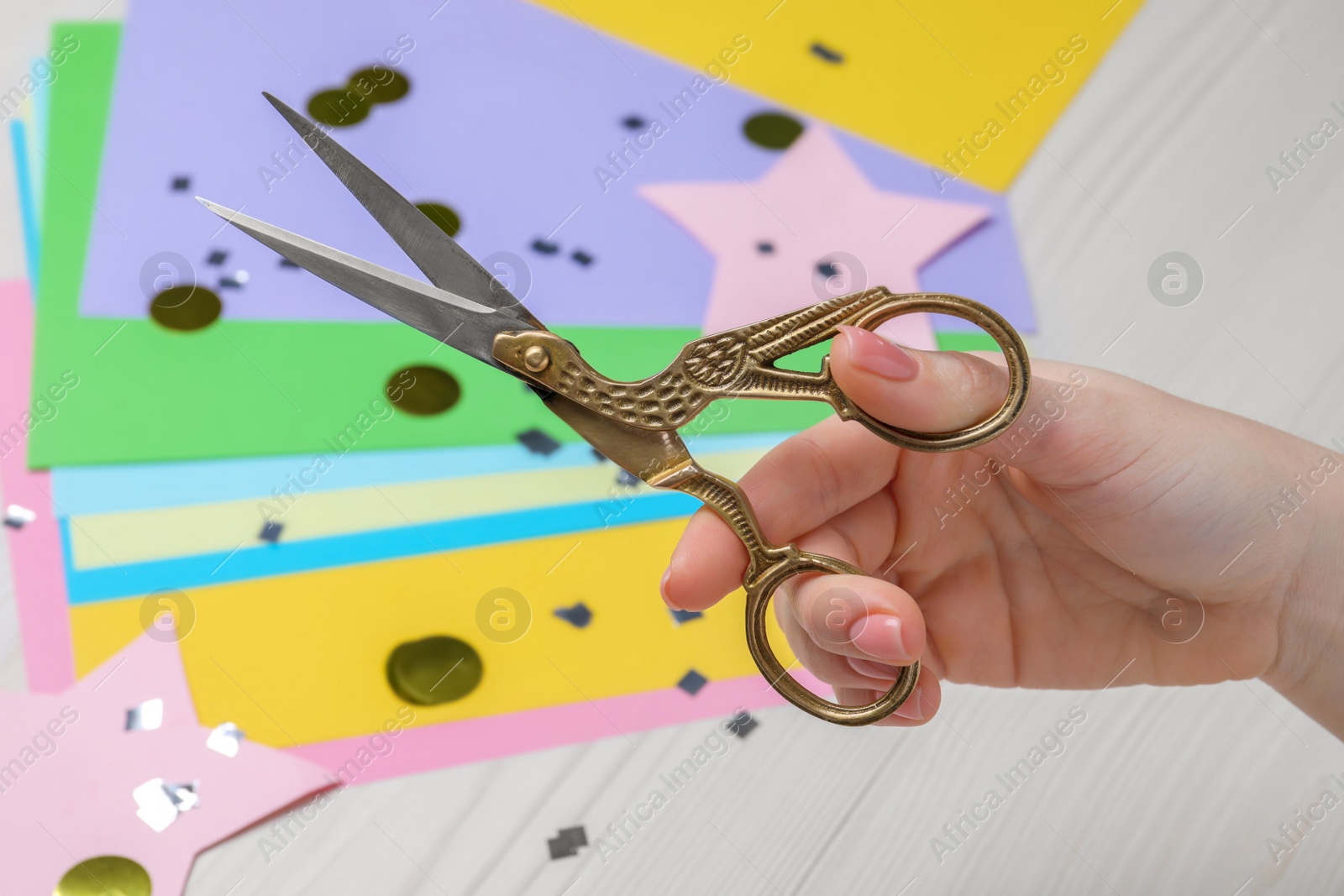 Photo of Woman holding scissors at white wooden table, top view