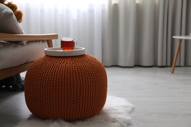 Photo of Tray with cup of tea on stylish knitted pouf in room. Interior design