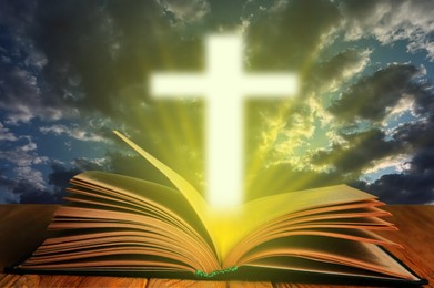 Silhouette of cross and open Bible on wooden table against cloudy sky