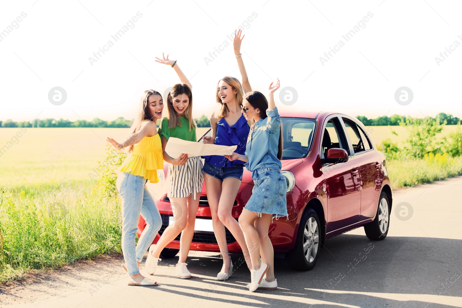 Photo of Happy beautiful young women with map standing near car in countryside