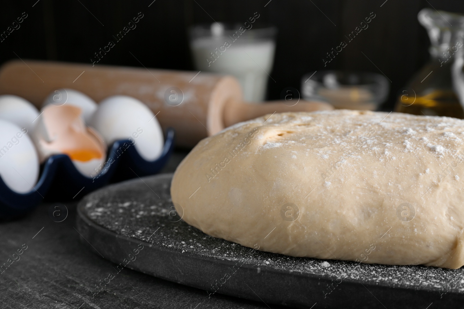 Photo of Fresh yeast dough with flour on black table, closeup