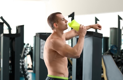 Photo of Athletic young man drinking protein shake in gym