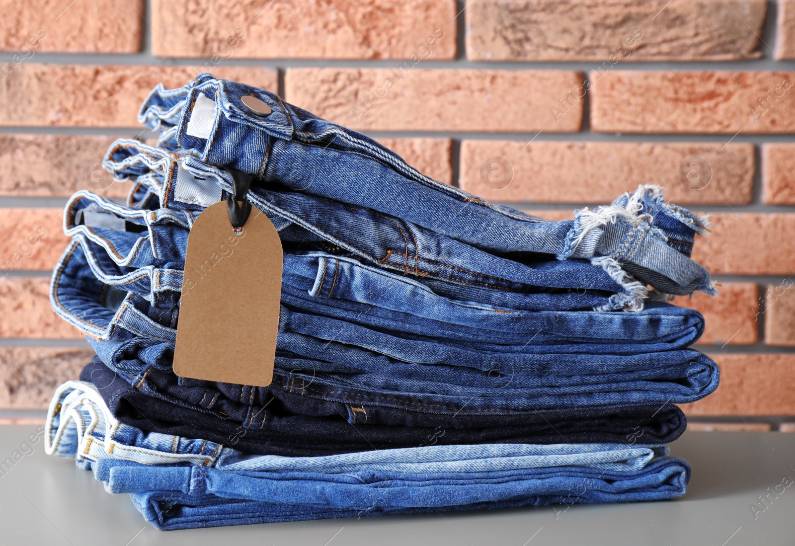 Photo of Stack of jeans on table against brick wall background