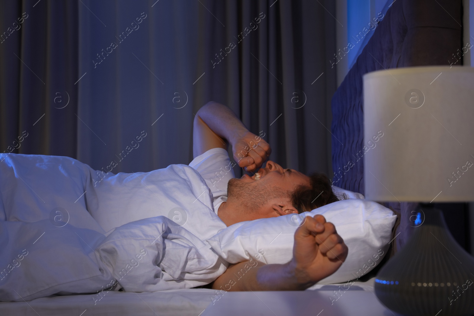 Photo of Handsome young man yawning while lying on pillow at night. Bedtime