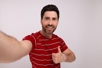 Photo of Smiling man taking selfie and showing thumbs up on white background