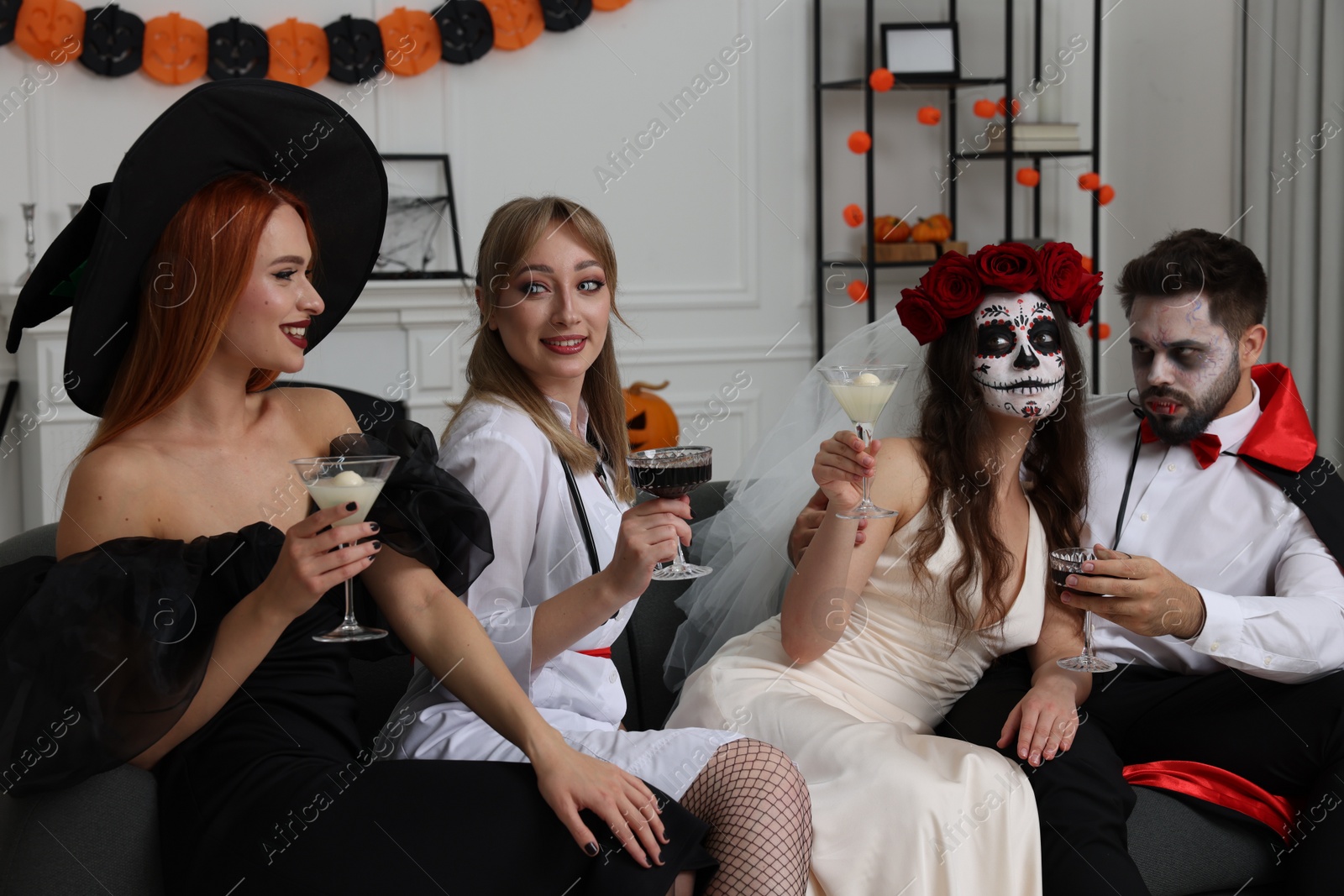 Photo of Group of people in scary costumes with cocktails celebrating Halloween indoors