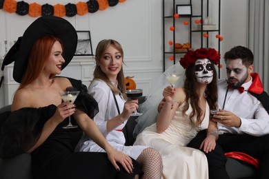 Group of people in scary costumes with cocktails celebrating Halloween indoors