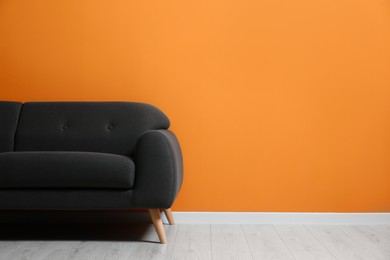 Photo of Stylish room with cosy sofa near orange wall, space for text. Interior design